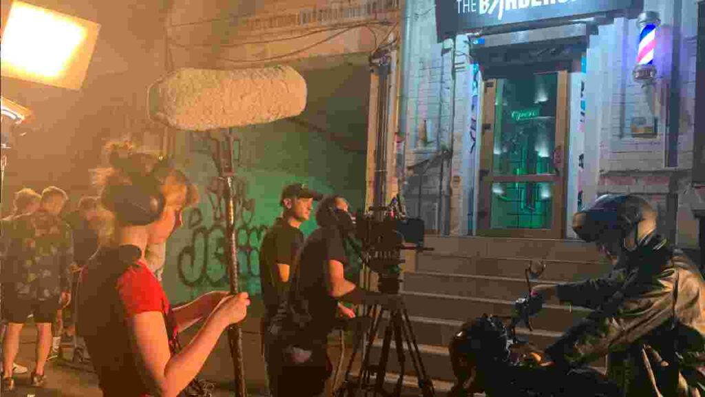 Sound operator on a night film set in Thailand recording clean audio with boom microphone during exterior video shoot.